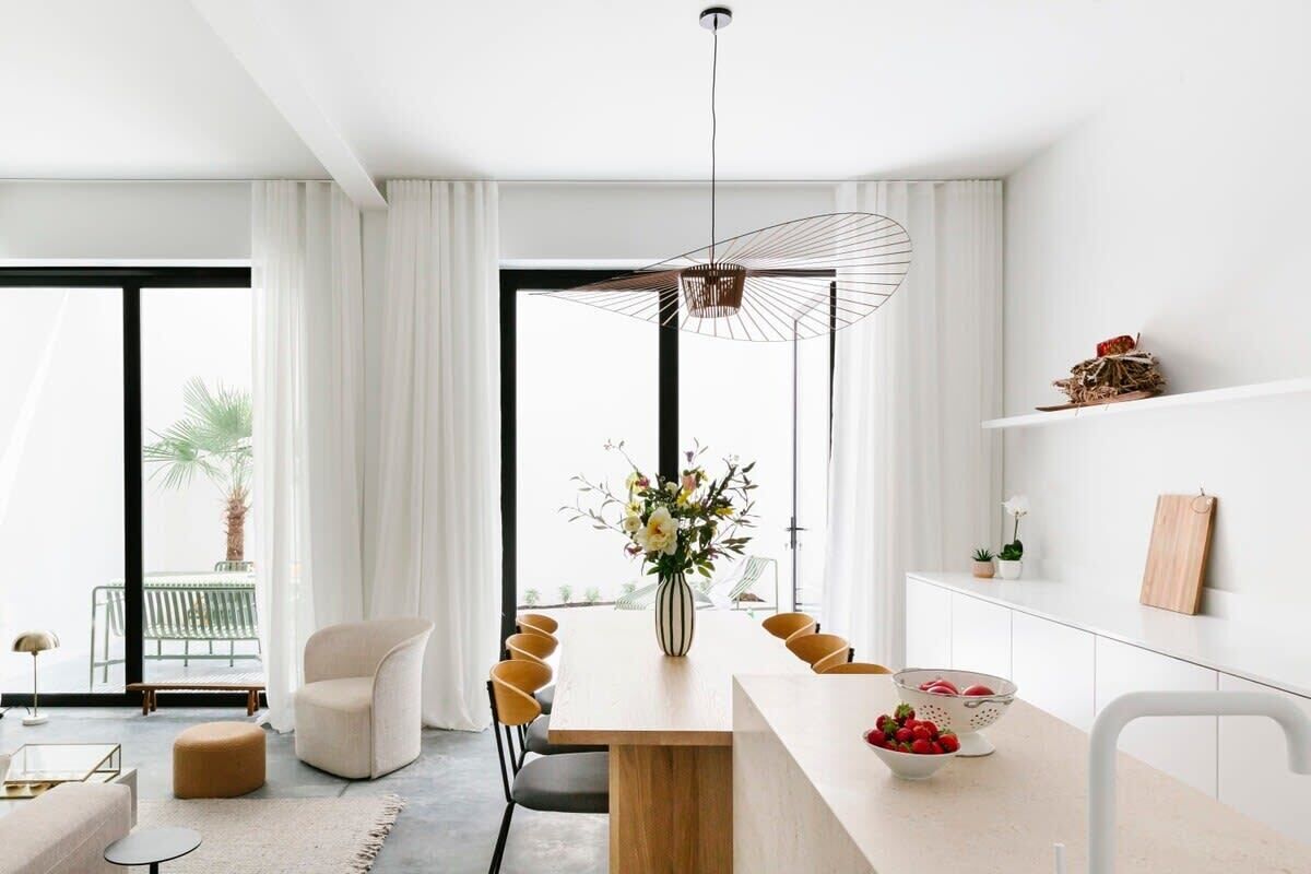 Een moderne eetruimte met een houten tafel, witte stoelen en een centrale vaas met bloemen.