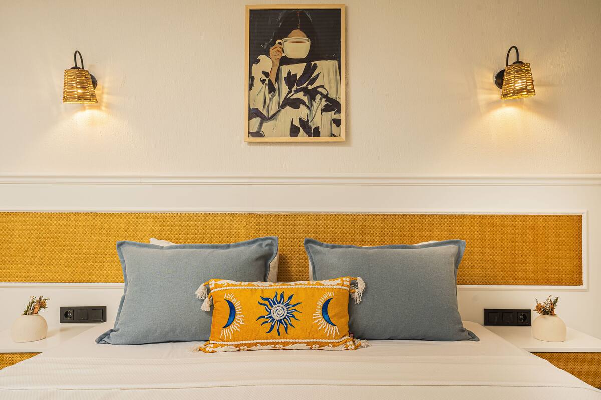A hotel room with a bed, two pillows, a wall-mounted artwork, and two wall sconces.