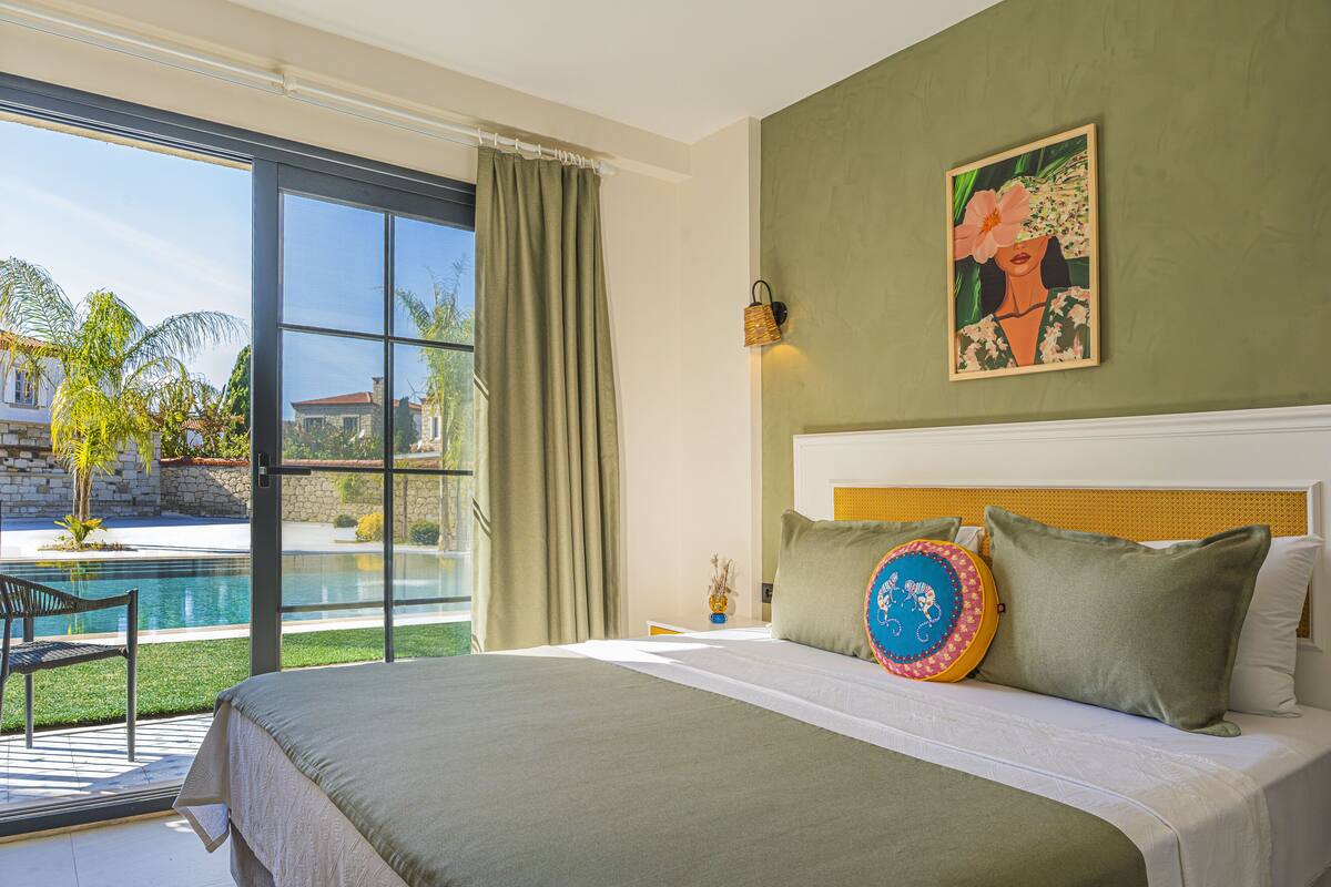 A bedroom with a large bed, a view of a swimming pool, and a painting on the wall.