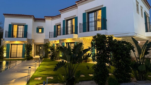 A multi-story residential building with a white facade, green shutters, and a stone base. - Lyse Jülide (Cesme)