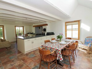 A spacious kitchen with a dining area, featuring a large island, wooden chairs, and a polka dot tablecloth. - Bryn Isaf (Tregaron)