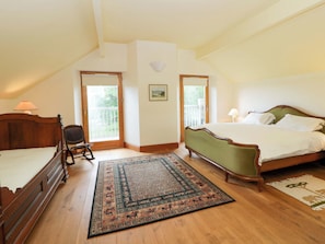 A bedroom with a wooden bed, a rocking chair, a large rug, and a balcony door. - Bryn Isaf (Tregaron)