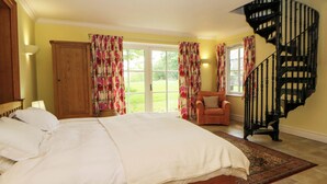 A bedroom with a large bed, a chair, a wooden wardrobe, a staircase, and a view of the outdoors. - Ty Cellin (Tregaron)