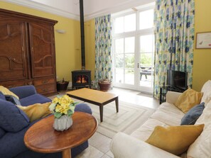 A living room with a sofa, a table with a vase, a television, a fireplace, and a view through a glass door. - Ty Cellin (Tregaron)