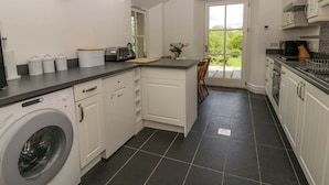A kitchen with a washing machine, a toaster, and a window with a view of greenery. - Ty Cellin (Tregaron)