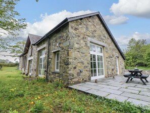 Un bâtiment en pierre doté d’un toit en pente, de grandes fenêtres et d’un patio avec une table.