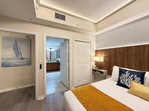 Een hotelkamer met een bed, nachtkastje, lamp, schilderij en uitzicht op de badkamer.