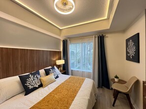 Habitación de hotel con una cama grande, un escritorio, una silla, una ventana con cortinas y una lámpara en el techo.