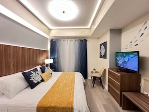 Quarto de hotel moderno com uma cama, uma televisão, uma escrivaninha e uma cadeira.