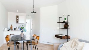 Ett modernt vardagsrum med ett runt matbord, trästolar, en soffa och en bokhylla.