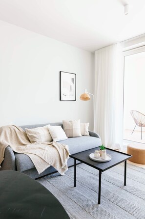 A modern living room with a grey sofa, a black coffee table, and a large window with sheer curtains. - Amazing 1BR apartment in Antwerp (Antwerpen)