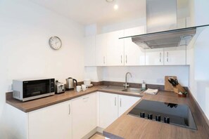 A modern kitchen with white cabinets, a microwave, a toaster, a kettle, and a sink. - Central Manchester 1BR Apartment with Balcony (Salford)