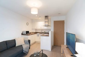 A compact living space with a kitchenette, a sofa, a TV, and a small dining area. - Central Manchester 1BR Apartment with Balcony (Salford)