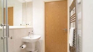 Un baño moderno con puerta de madera, cabina de ducha de vidrio y lavamanos blanco.