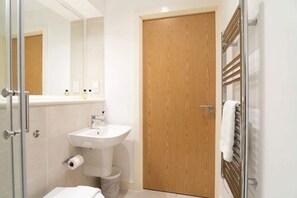 Ein modernes Badezimmer mit Holztür, einer Duschkabine aus Glas und einem weißen Waschbecken.