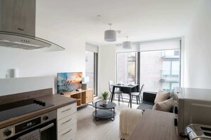 A modern kitchen with a built-in stove, a dining area with a table and chairs, and a sofa. - Central Manchester 1BR Apartment with Balcony (Salford)
