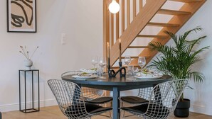 Un comedor con una mesa redonda, sillas de estructura metálica, una lámpara colgante moderna y una escalera al fondo.