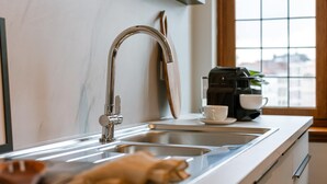 Una cocina moderna con un lavamanos de acero inoxidable, una cafetera y un ventanal con vistas a edificios.