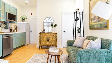 Un espace de vie compact comprenant un coin cuisine, un canapé vert, une commode décorative et un tableau accroché au mur.