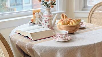 A dining table with a book, teapot, and pastries, set against a window with a view of buildings.
