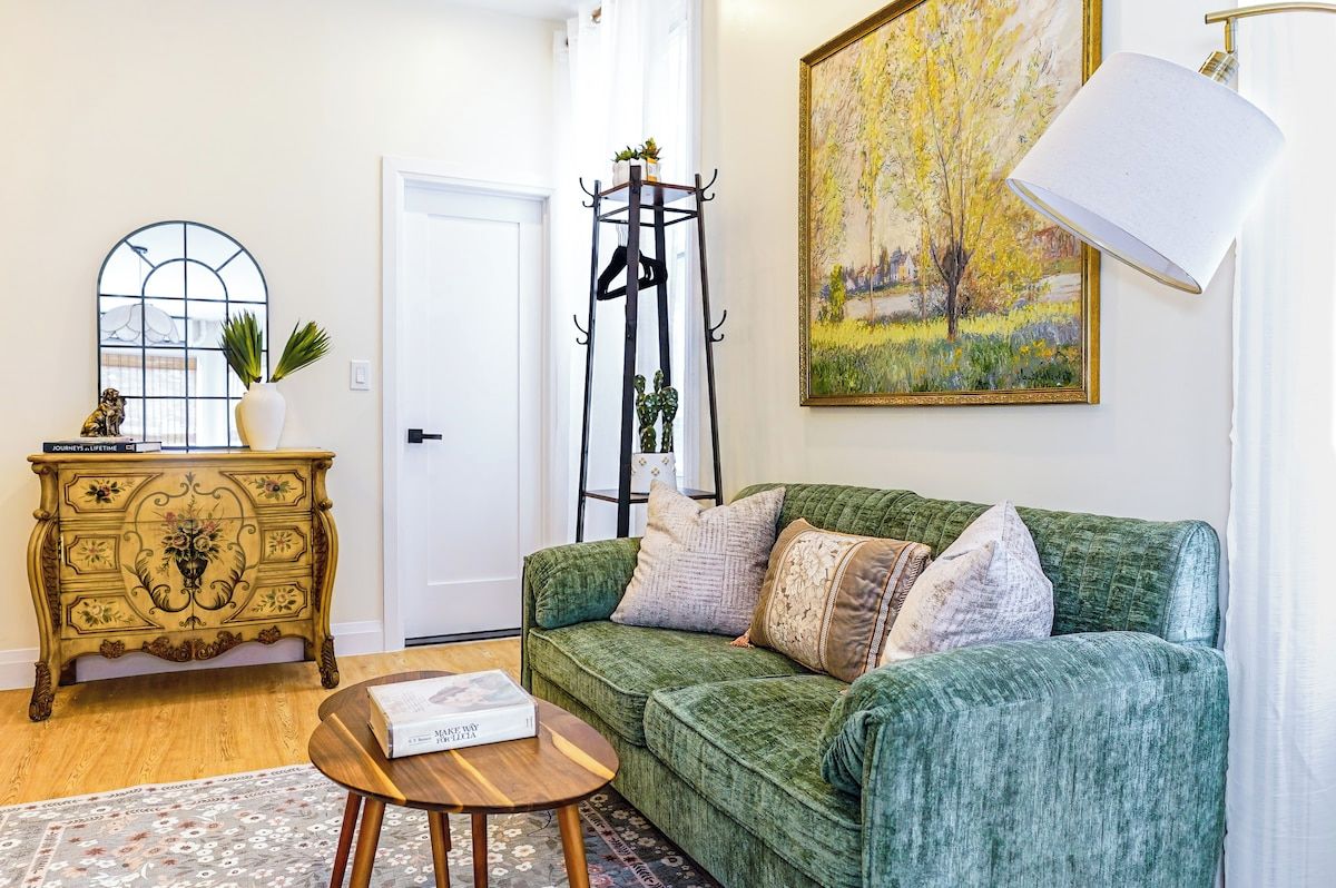 A living room with a green sofa, a wooden coffee table, a decorative cabinet, a floor lamp, and a painting on the wall.