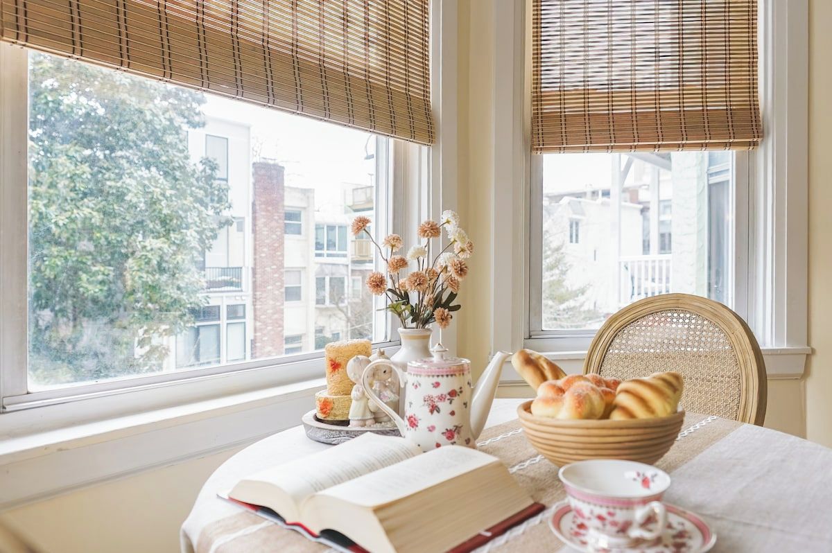 A room with a table set for tea, a book, and a vase with flowers.