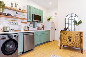 A compact kitchen with teal cabinets, a microwave, a dishwasher, and a vintage-style cabinet with floral designs. - A Slow Morning in a Parisian Studio (Philadelphia)