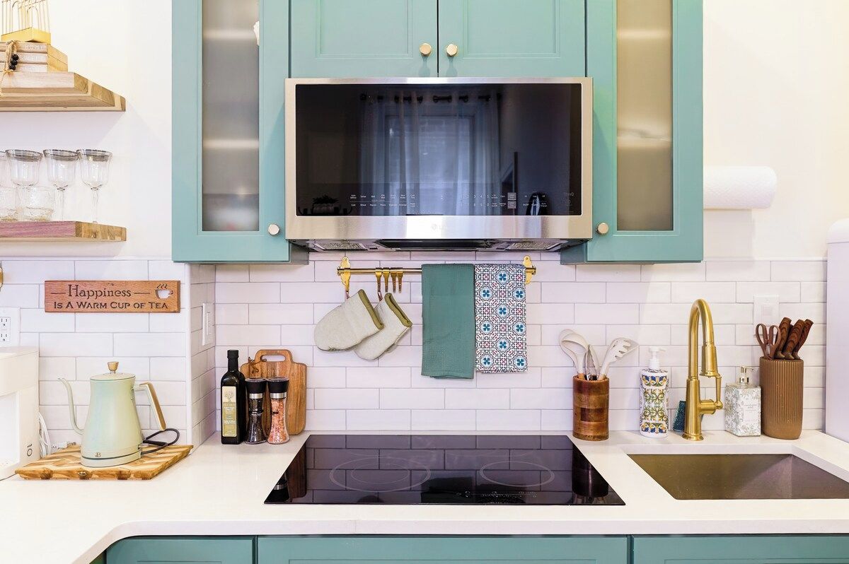 A kitchen with teal cabinets, a stainless steel microwave, and a black stove.