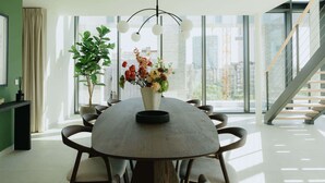 A modern dining area with a round table, chairs, a vase of flowers, and a staircase in the background. - Luxurious City Penthouse with Panoramic Terrace (Antwerpen)