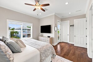 Une chambre à coucher avec un lit, un ventilateur de plafond, une télévision et une vue sur l’extérieur.