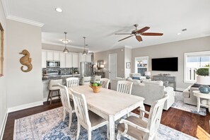 A modern kitchen with white cabinets, a dining area with a wooden table and chairs, and a living room with a sofa and a TV. - Newly Furnished | LSV | Community Pool (Santa Rosa Beach)