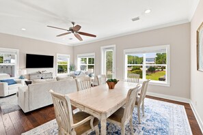 A spacious living room with a dining area, a ceiling fan, and large windows offering a view of the outdoors. - Newly Furnished | LSV | Community Pool (Santa Rosa Beach)