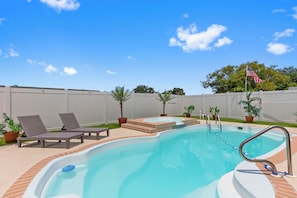 Uma piscina com espreguiçadeiras, uma banheira de hidromassagem e uma bandeira americana.