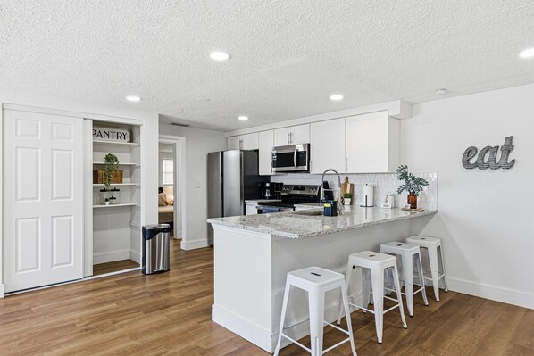 A modern kitchen with white cabinetry, a granite countertop, and a central island with bar stools.