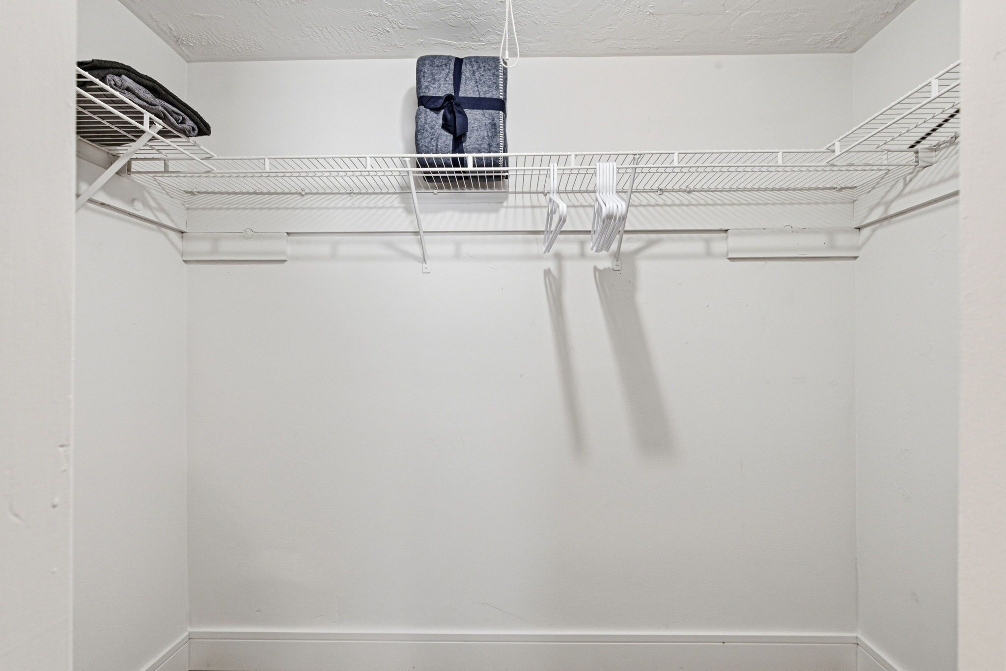 A white closet with a metal shelf and a towel hanging on the wall.