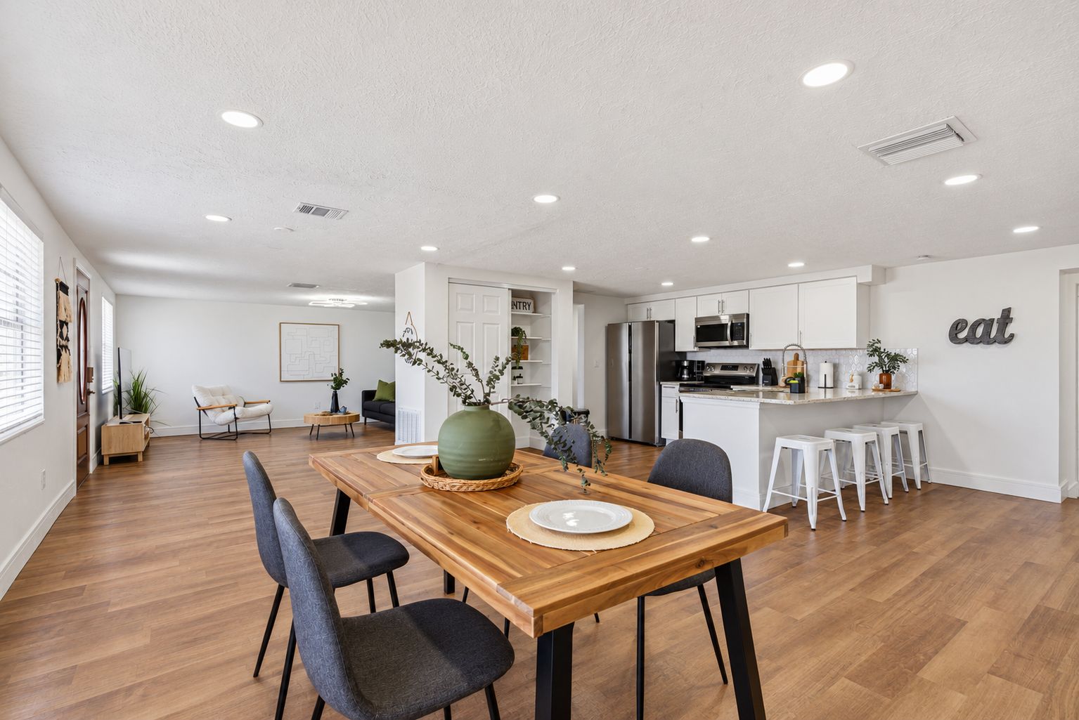 A spacious living area with a wooden dining table, modern kitchen, and a large window.