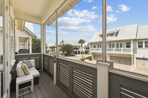A covered porch with a seating area, overlooking a residential street with houses and a clear sky. - Fitness Facility | Pool Access | Garage (Panama City)