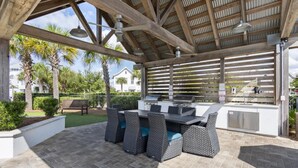 Un patio exterior con una parrilla, mobiliario de mimbre y un área cubierta con techo de madera.
