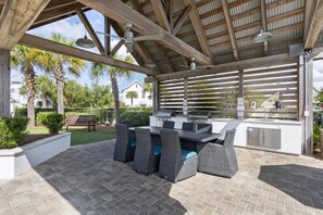 Eine Außenpatio mit Grill, Korbmöbeln und einem überdachten Bereich mit Holzboden.