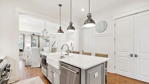 Een moderne keuken met roestvrijstalen apparatuur, een centraal eiland, hanglampen en uitzicht op de eetruimte.