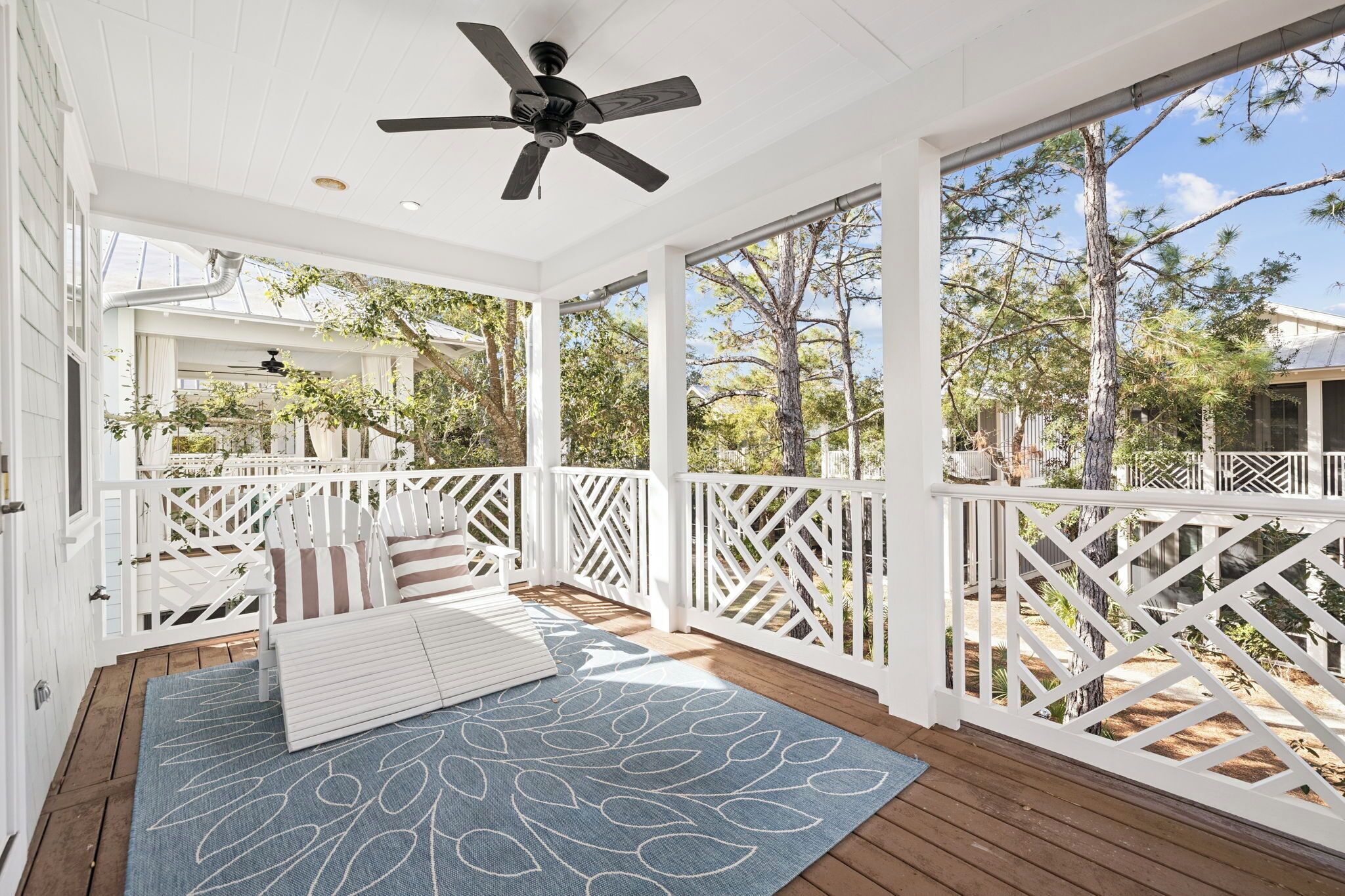 A covered porch with white railings, a ceiling fan, and a view of trees and sky.