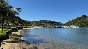 A beach with clear water, palm trees, and boats docked near a pier. - Apartment at Costabella Resort in Angra dos Reis (Angra dos Reis)