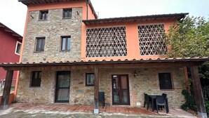 A two-story stone building with a flat roof, a covered patio area, and a small outdoor seating arrangement. - Apartment 'Casa La Corte in Capannori' with Private Pool, Wi-Fi & Air Conditioning (Capannori)