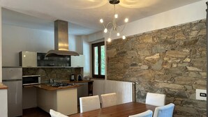A modern kitchen with a stone wall, a dining table with chairs, and a chandelier. - Apartment 'Casa La Corte in Capannori' with Private Pool, Wi-Fi & Air Conditioning (Capannori)