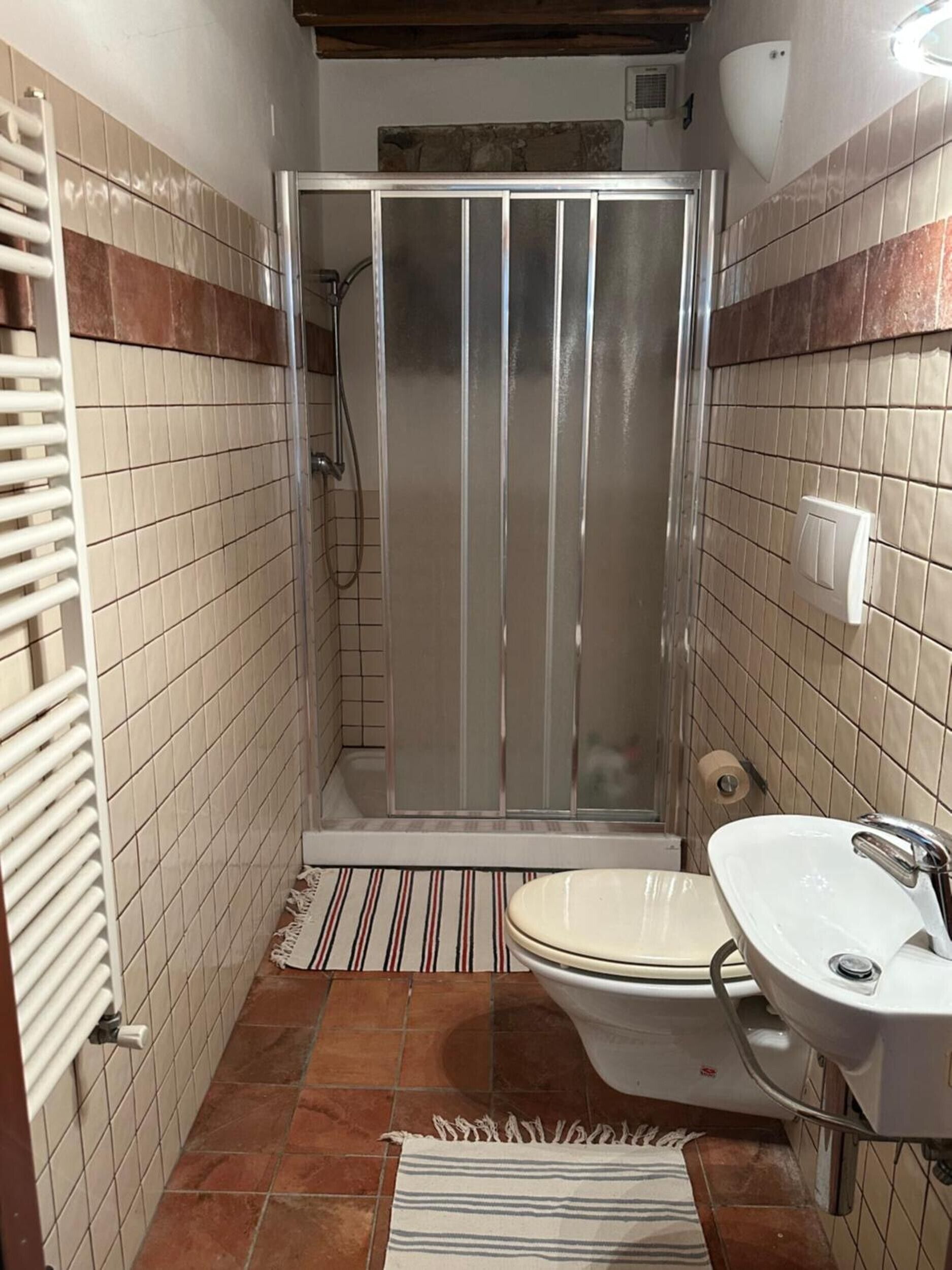 Une salle de bain avec une douche, des toilettes, un lavabo et un tapis rayé sur le sol.