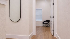 Um corredor com piso de madeira, uma porta branca e uma cadeira preta dobrável.