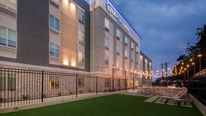 Un hôtel doté d’une façade moderne, d’un espace extérieur aménagé pour s’asseoir et d’une entrée bien éclairée.