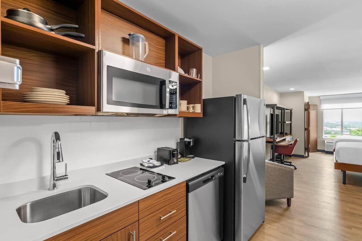 A modern kitchen with a stainless steel sink, microwave, and refrigerator, wooden shelves, and a view of the city.