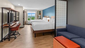 Une chambre d’hôtel avec un lit, un bureau avec un ordinateur, un canapé bleu et une fenêtre donnant sur un beau paysage.