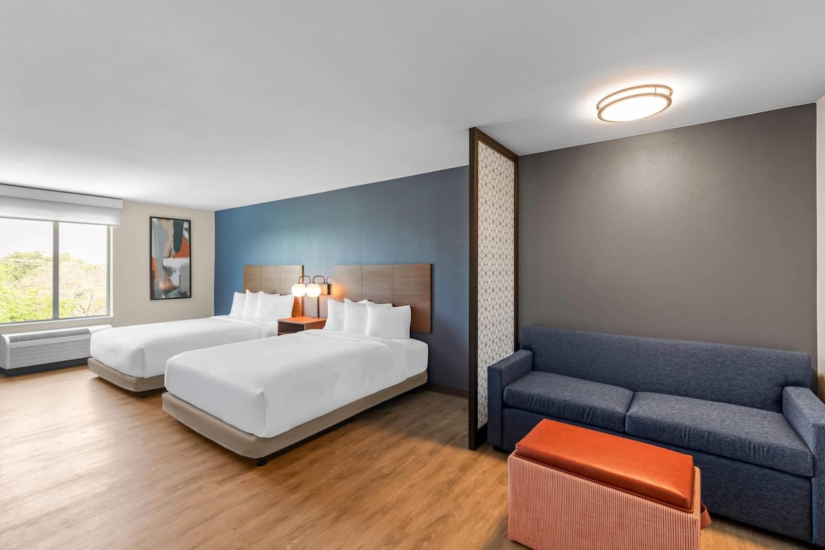 A hotel room with two beds, a sofa, a small table, and a large window.